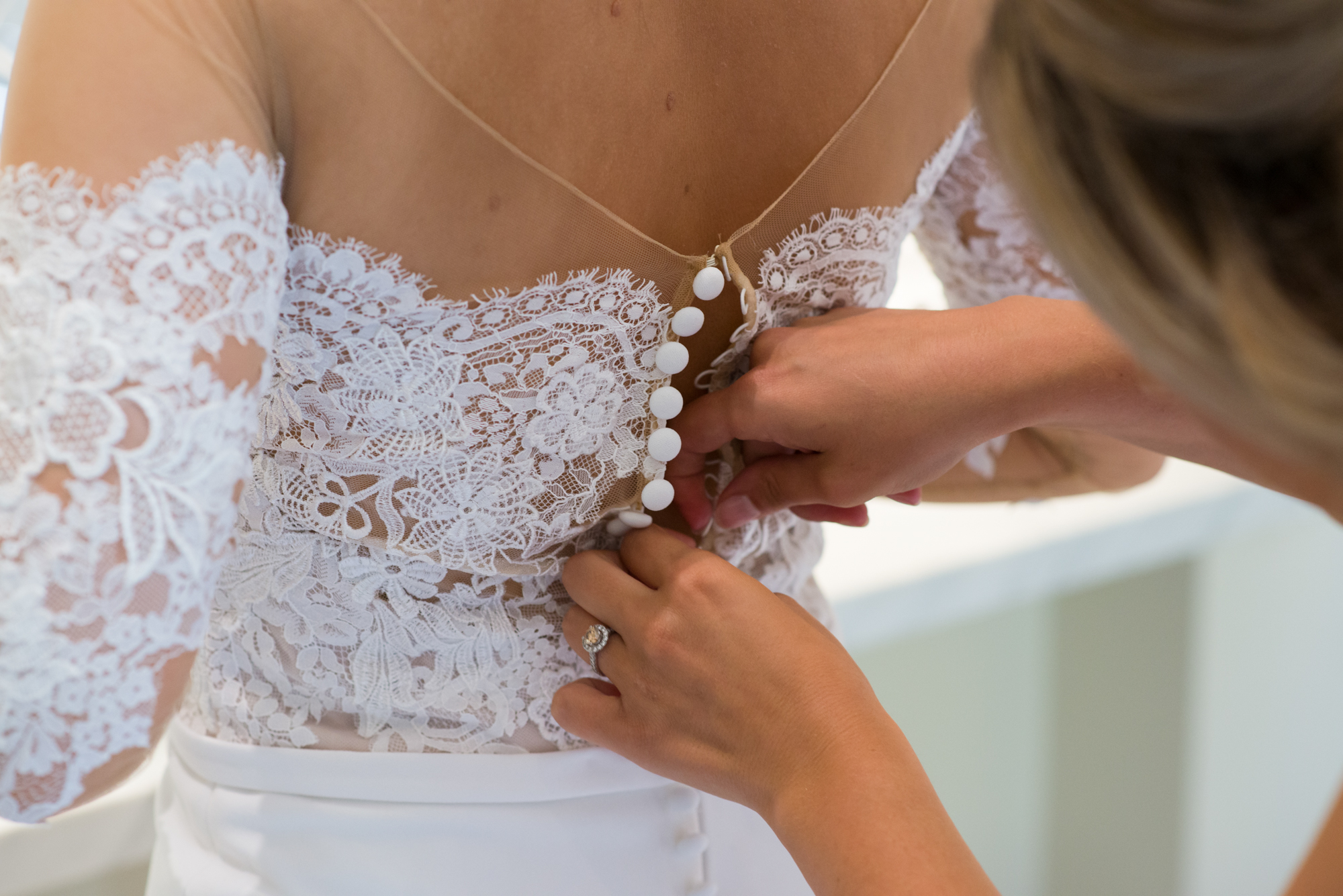 A bride having the back of her white lace pronovias dress buttoned up